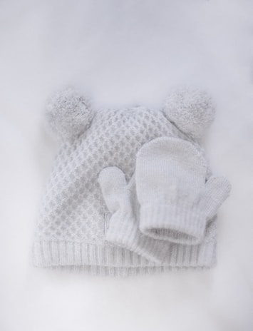 A cozy celeste-colored knitted baby hat with a small pom-pom on top.