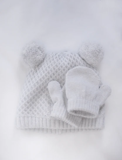 Close-up of knitted mittens and a matching hat set in gentle earth tones for kids.