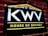 A dark rectangular sign on a brick wall features bold white letters 'KWV' above the words 'House of Brandy' in bright yellow. The sign is bordered by a yellow line on the top, forming a subtle triangular shape resembling a roof, and another line below the text.
