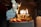 A decorated cake topped with strawberries and gold candles spelling out 'BIRTHDAY' is lit, with sparklers adding a festive touch. In the background, people are gathered, creating a cozy and celebratory atmosphere.