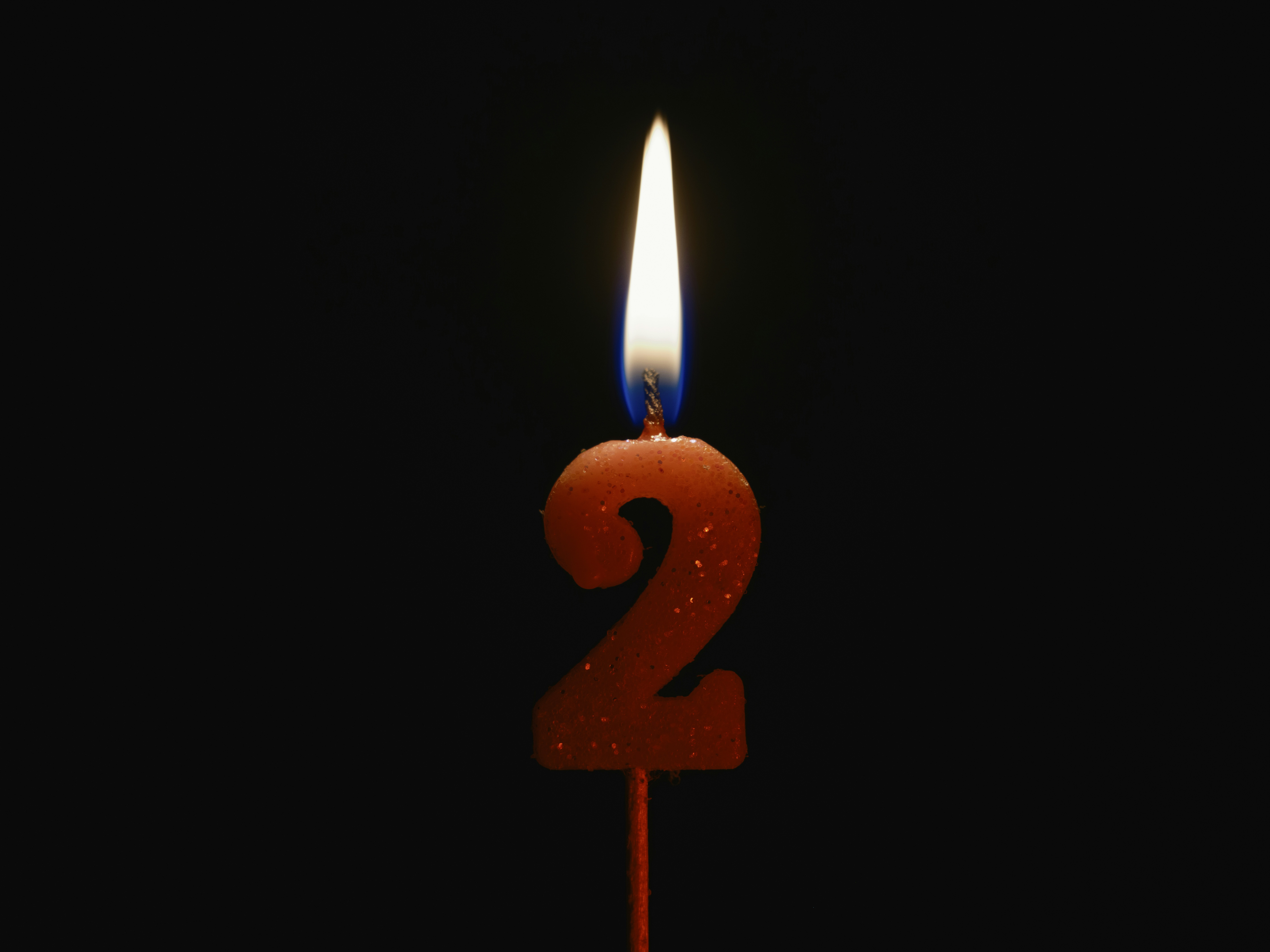 Burning birthday candle isolated on black background, number 2