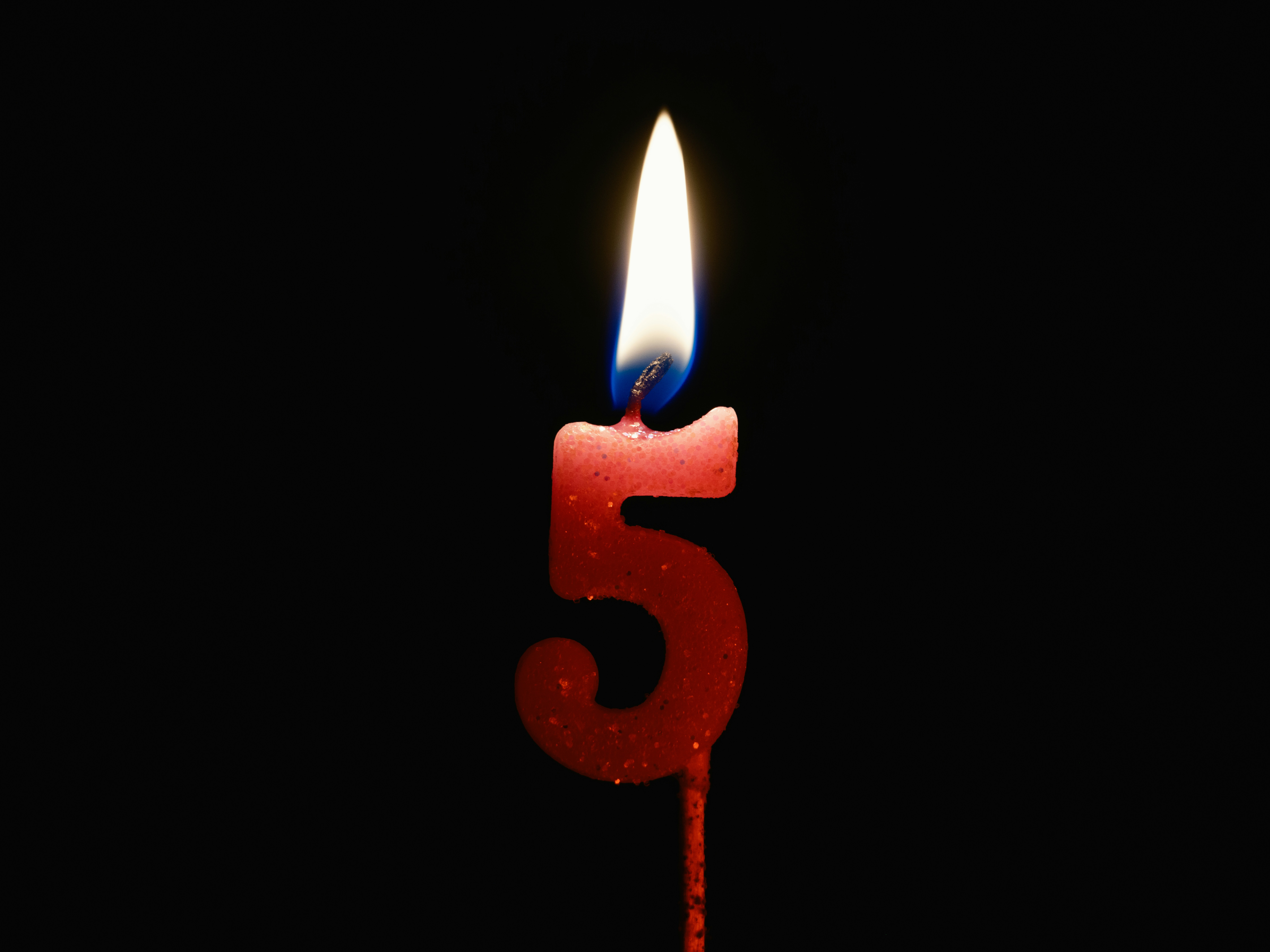 Burning birthday candle isolated on black background, number 5