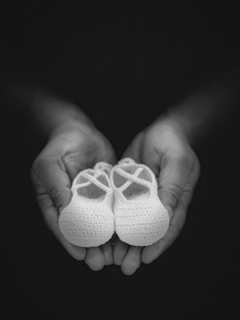 Hands holding a tiny pair of baby shoes gently.