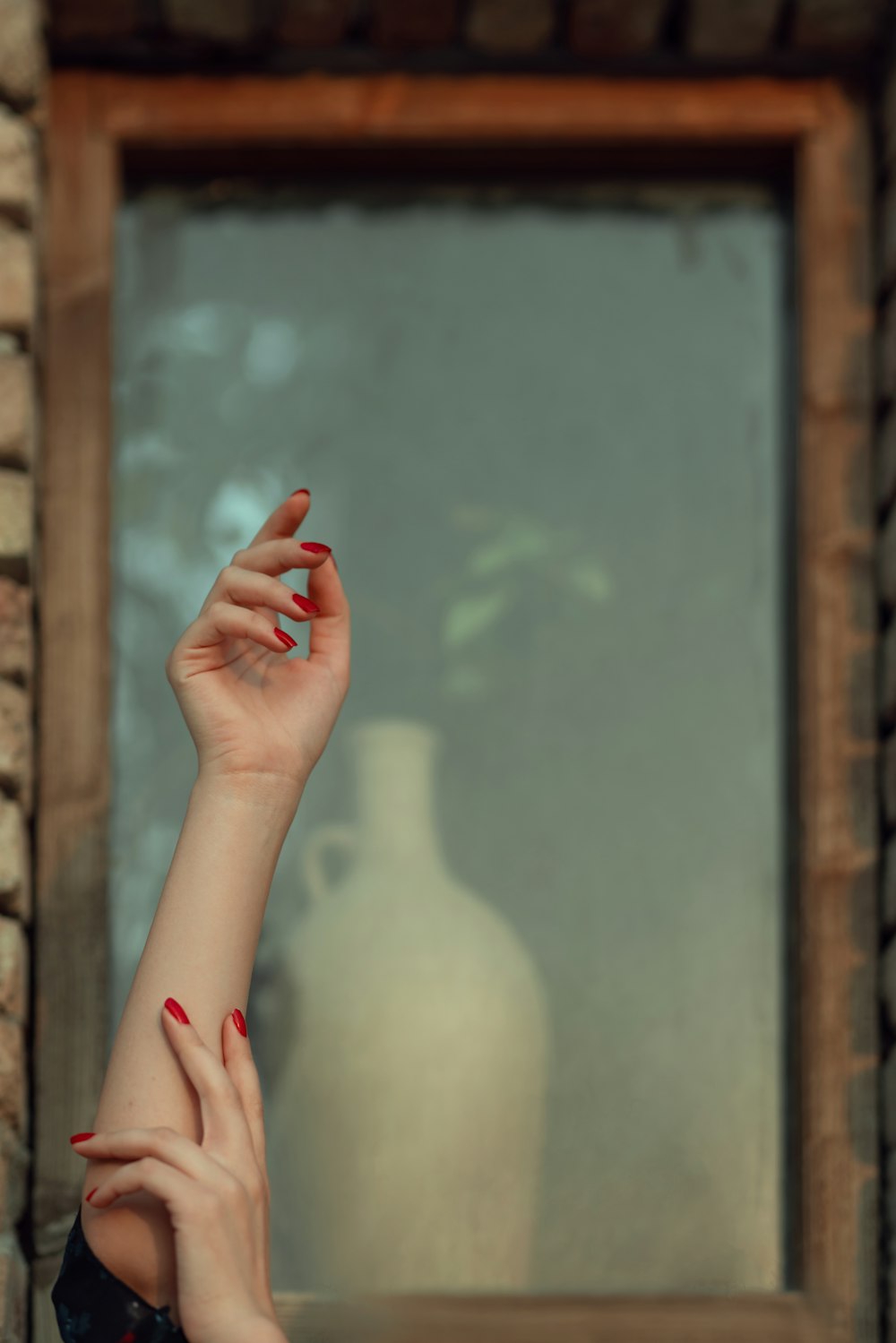 a woman with red nail polish holding her hand up in front of a window