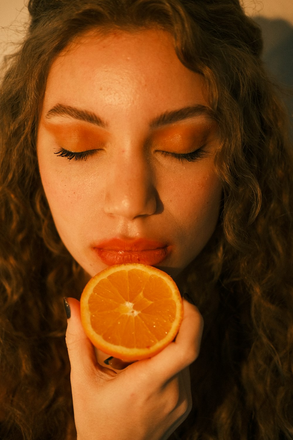 a woman is holding an orange slice to her mouth
