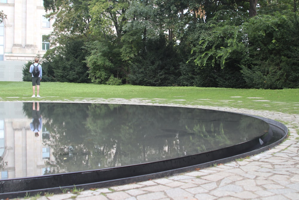 Un uomo in piedi di fronte a una piscina riflettente in un parco