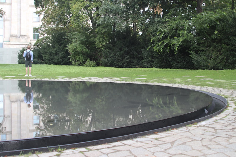 a man standing in front of a reflecting pool in a park