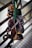 A collection of climbing equipment, including carabiners and belay devices, is hanging from a railing. The gear is attached to a green strap, showcasing several metallic items primarily in silver and gold tones.