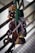 A collection of climbing equipment, including carabiners and belay devices, is hanging from a railing. The gear is attached to a green strap, showcasing several metallic items primarily in silver and gold tones.