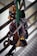 A collection of climbing equipment, including carabiners and belay devices, is hanging from a railing. The gear is attached to a green strap, showcasing several metallic items primarily in silver and gold tones.