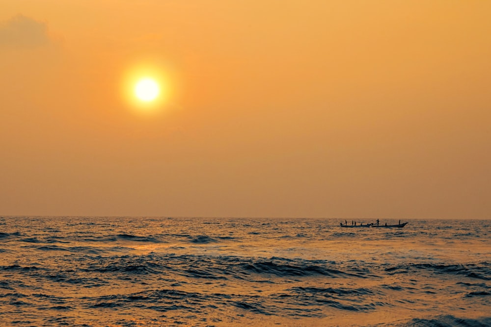 the sun is setting over the ocean with a boat in the water