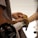 A person operates a lathe machine to shape a wooden object, holding sandpaper to smooth the surface. The image focuses on the craftsmanship involved in woodworking.