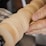 A close-up view of a hand holding sandpaper against a spinning wooden object, possibly on a lathe. The motion blur on the wood indicates it is rotating at a high speed.