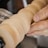 A close-up view of a hand holding sandpaper against a spinning wooden object, possibly on a lathe. The motion blur on the wood indicates it is rotating at a high speed.