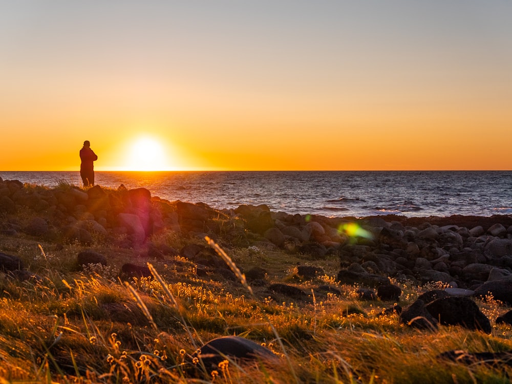 岩だらけの海岸に立って夕日を見ている人