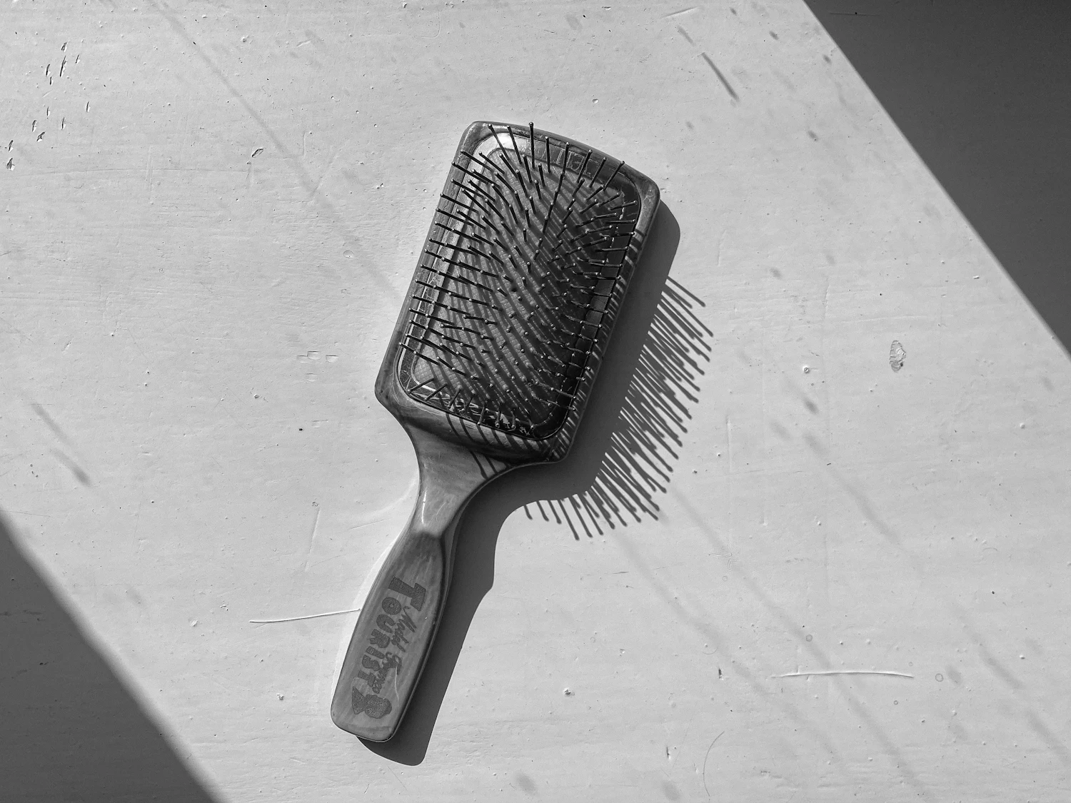 A flat paddle brush casting a hard shadow across a white surface