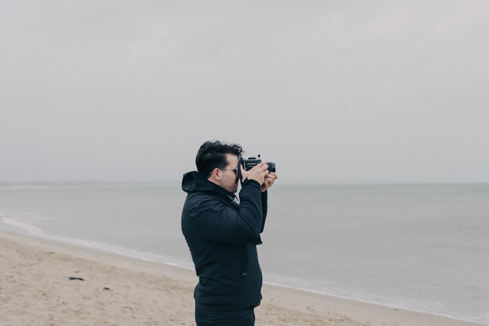 um homem em pé em uma praia tirando uma foto do oceano