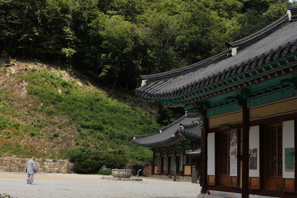 a woman walking down a street next to a lush green hillside