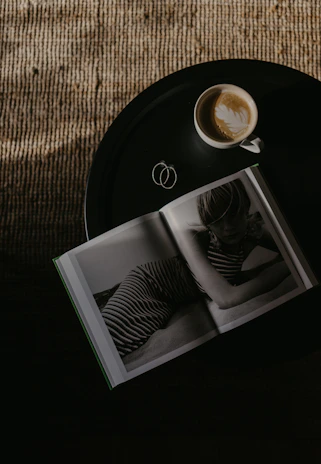 A snapshot of a café table with a latte, open book, and a Polaroid photo pinned to a corkboard.