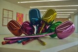 A sculpture composed of several metallic, colorful balloon-like tulips arranged on a platform, set in a modern gallery space with minimalistic design and framed artworks on the walls.