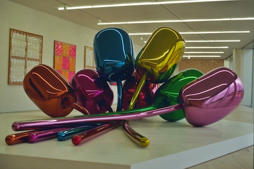 A sculpture composed of several metallic, colorful balloon-like tulips arranged on a platform, set in a modern gallery space with minimalistic design and framed artworks on the walls.