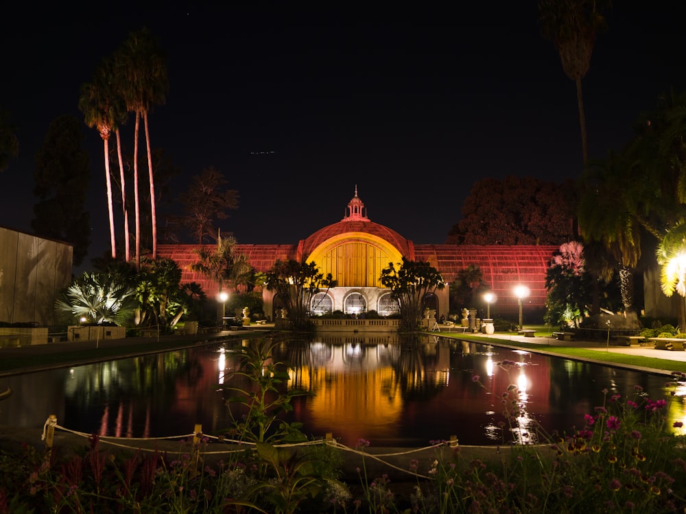 a building lit up at night with a pond in front of it