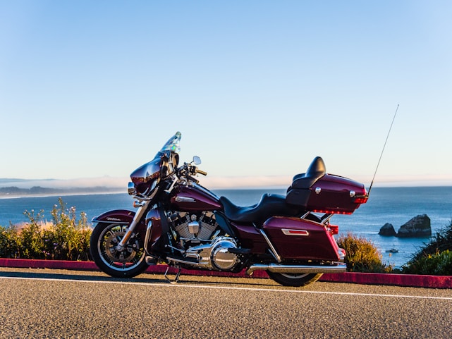 A sleek motorbike parked on a sunlit Bali beach road with palm trees and ocean waves in the background.