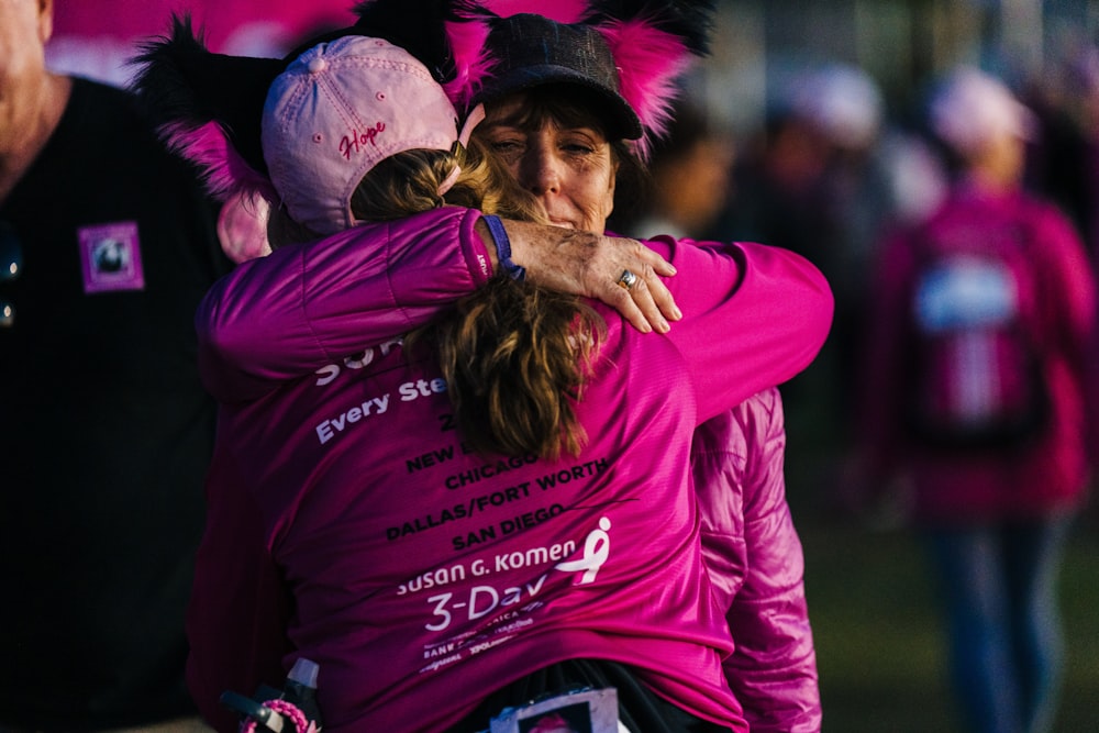 a woman in a pink shirt hugging another woman