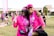 Two people are smiling and posing together outdoors, wearing matching bright pink shirts and accessories, possibly participating in a charity event or walk. Both individuals appear happy and relaxed, and there are other participants and banners in the background, suggesting a lively and supportive atmosphere.