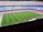 A large football stadium with empty seats arranged in vibrant blue and maroon colors. The well-maintained green field is visible, and a small group of people are gathered near one side of the field. The phrase 'MÉS QUE UN CLUB' is prominently displayed in yellow on the seats.