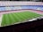 A large football stadium with empty seats arranged in vibrant blue and maroon colors. The well-maintained green field is visible, and a small group of people are gathered near one side of the field. The phrase 'MÉS QUE UN CLUB' is prominently displayed in yellow on the seats.