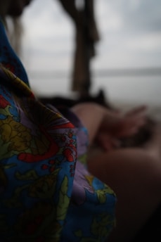 A colorful patterned fabric is in focus, with a blurred background that includes a person with an outstretched arm and a dim outdoor setting.