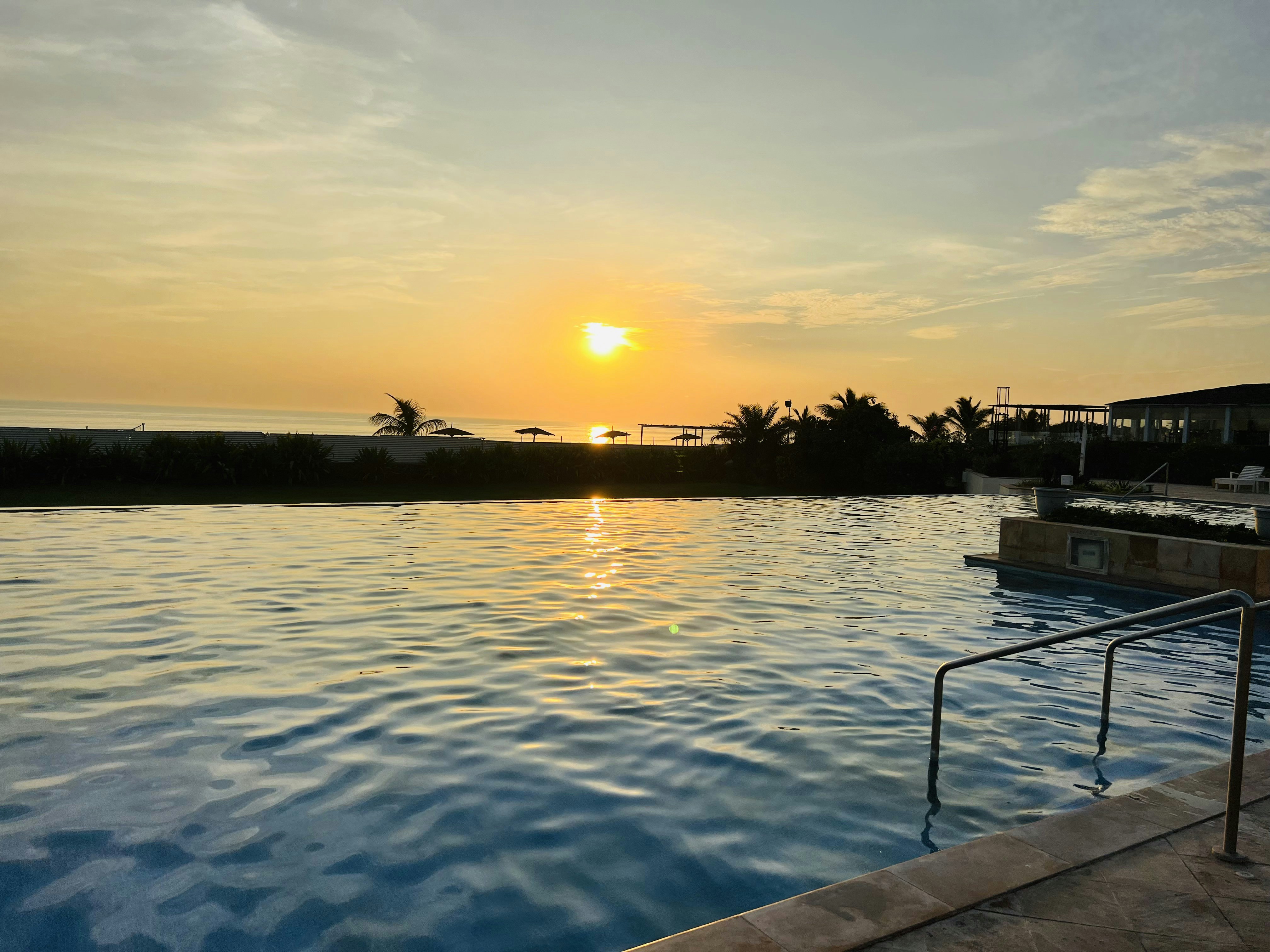 Infinity pool at sunset overlooking the sea, warm golden light, lounge chairs, still water reflection