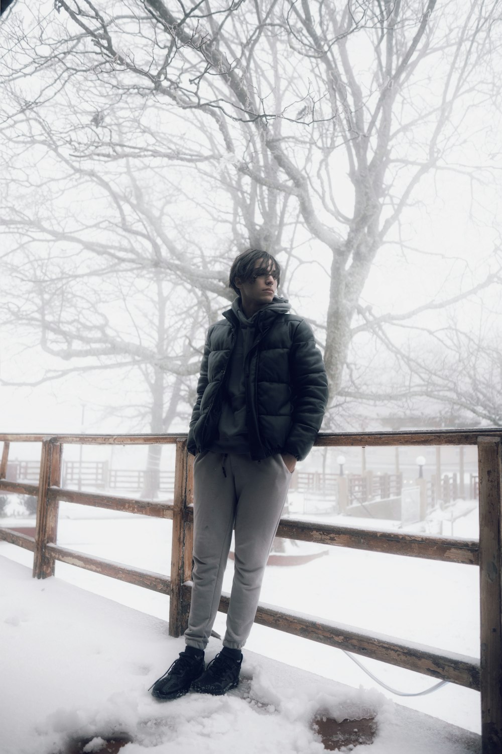 a woman standing in the snow next to a fence