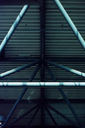 Metal beams intersect with corrugated metal panels creating a structured, geometrical pattern. Shadows play across the horizontal lines, adding depth and contrast.