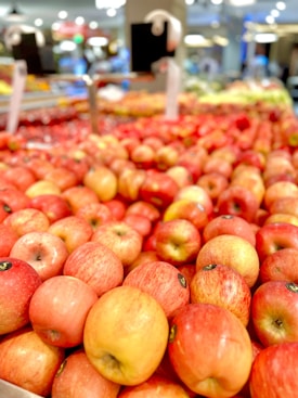 A vibrant display of fresh apples in various shades of red and yellow is neatly arranged in a market setting. The scene is bustling with produce, indicating a well-stocked and busy grocery store. The image is slightly blurred in the background, suggesting depth and a focus on the apples.