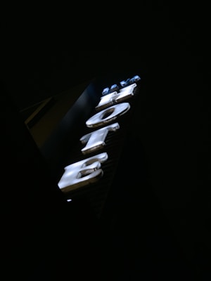 Illuminated hotel sign with large, bold letters glowing against a dark background. The sign is vertically oriented and the letters are white with a slight blue tint.