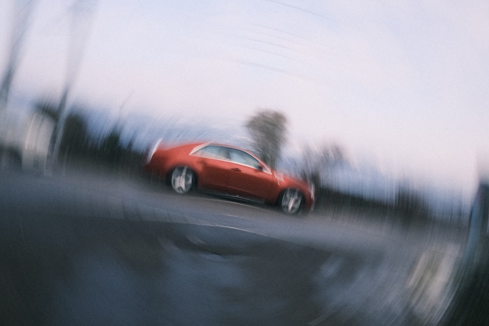a red car driving down a street next to a forest