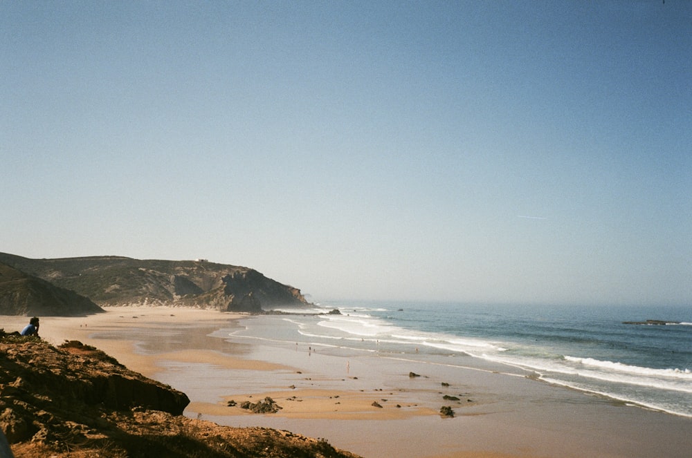 a person sitting on a cliff overlooking a beach