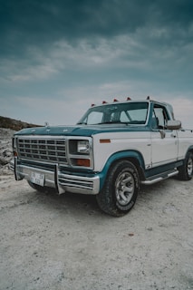 A rich, editorial-style photograph of a vintage pickup truck parked under a wide western sky with shadowed clouds.