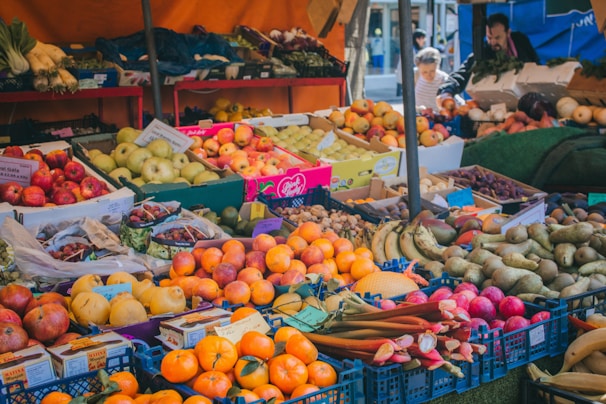 A vibrant farmers market stall filled with fresh fruits and vegetables under a sunny sky.