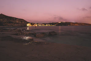 A quiet coastal village at dusk, with pastel skies and gentle waves.