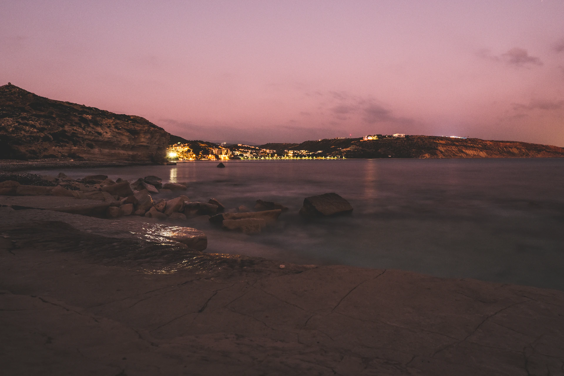 A serene coastal view at dusk, with gentle waves lapping against weathered rocks under a pastel sky.