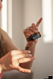 Hand pouring herbal oil into a small bottle surrounded by fresh leaves.