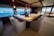 A luxurious interior space featuring a large, elegant bar counter surrounded by plush, comfortable armchairs. The room is well-lit with soft lighting fixtures above, and large windows provide a clear view of a scenic ocean vista. The decor feels sophisticated and upscale with polished wood and neutral tones. A bouquet of flowers can be seen on the far end of the counter, adding a touch of freshness to the setting.