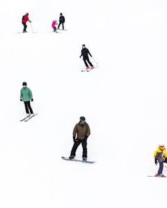 Several people are skiing and snowboarding on a snowy slope. The individuals are dressed in winter gear, including helmets and goggles. The snow is bright and seems freshly fallen, contrasting with the vibrant colors of the clothing.