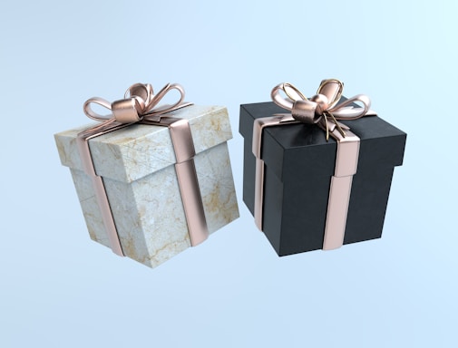 Two neatly wrapped gift boxes, one with a marble texture and the other in black, each adorned with a shiny rose gold ribbon and bow, set against a light blue background.