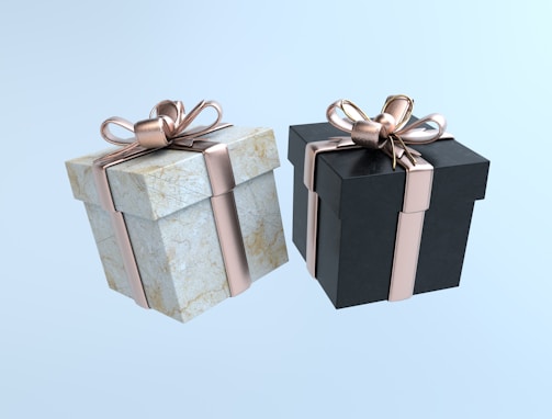 Two neatly wrapped gift boxes, one with a marble texture and the other in black, each adorned with a shiny rose gold ribbon and bow, set against a light blue background.