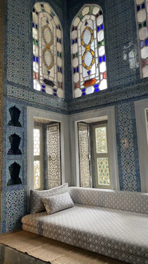 A serene, light-filled room with soft ceramic blue walls and warm white accents, featuring a cozy seating area with textured Lisbon tiles.