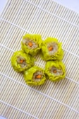 Five pieces of yellow dumplings with a filling that appears to contain minced meat and small orange carrot cubes, arranged neatly on a bamboo sushi mat. The dumplings are placed in a circular pattern, creating an aesthetically pleasing presentation.